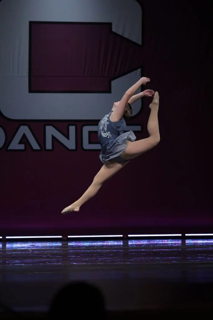 a student who is a ballerina leaps throug the air on stage.