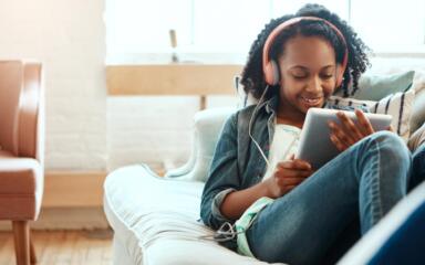 Student wearing a pink pair of headphones while using their tablet